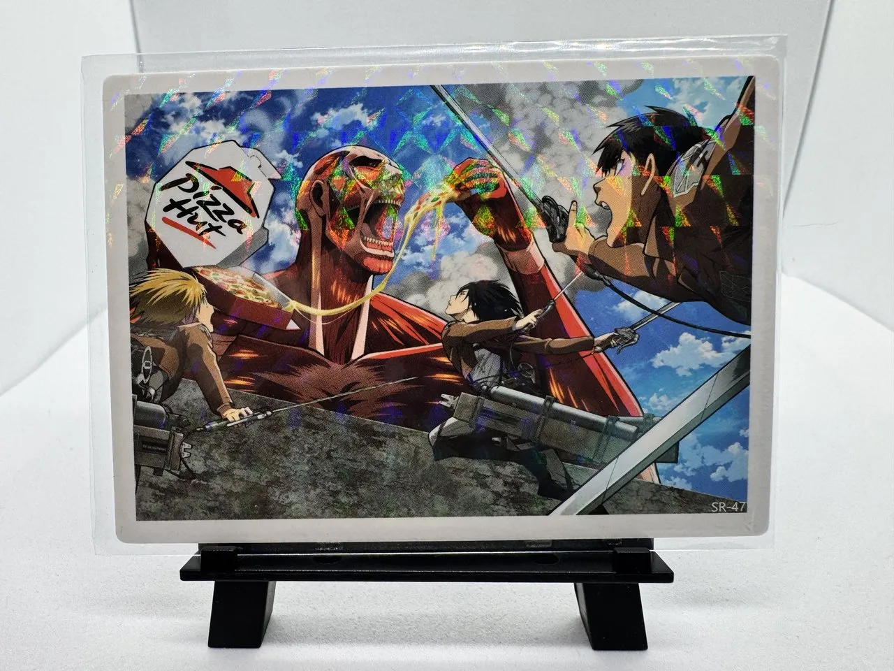 An Attack on Titan foil card showing the Colossal Titan eating a slice of pizza from a Pizza Hut box while the Scouts attack, card number SR-47